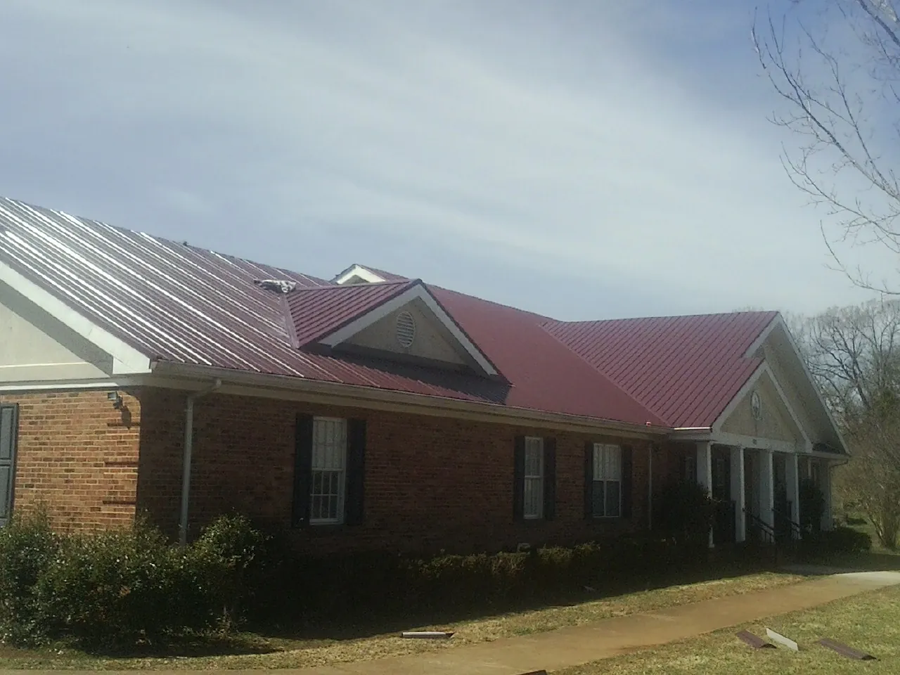 Red metal roof with gabled entries on a long brick building, from a Hail Damage Roof Repair job in Urbana