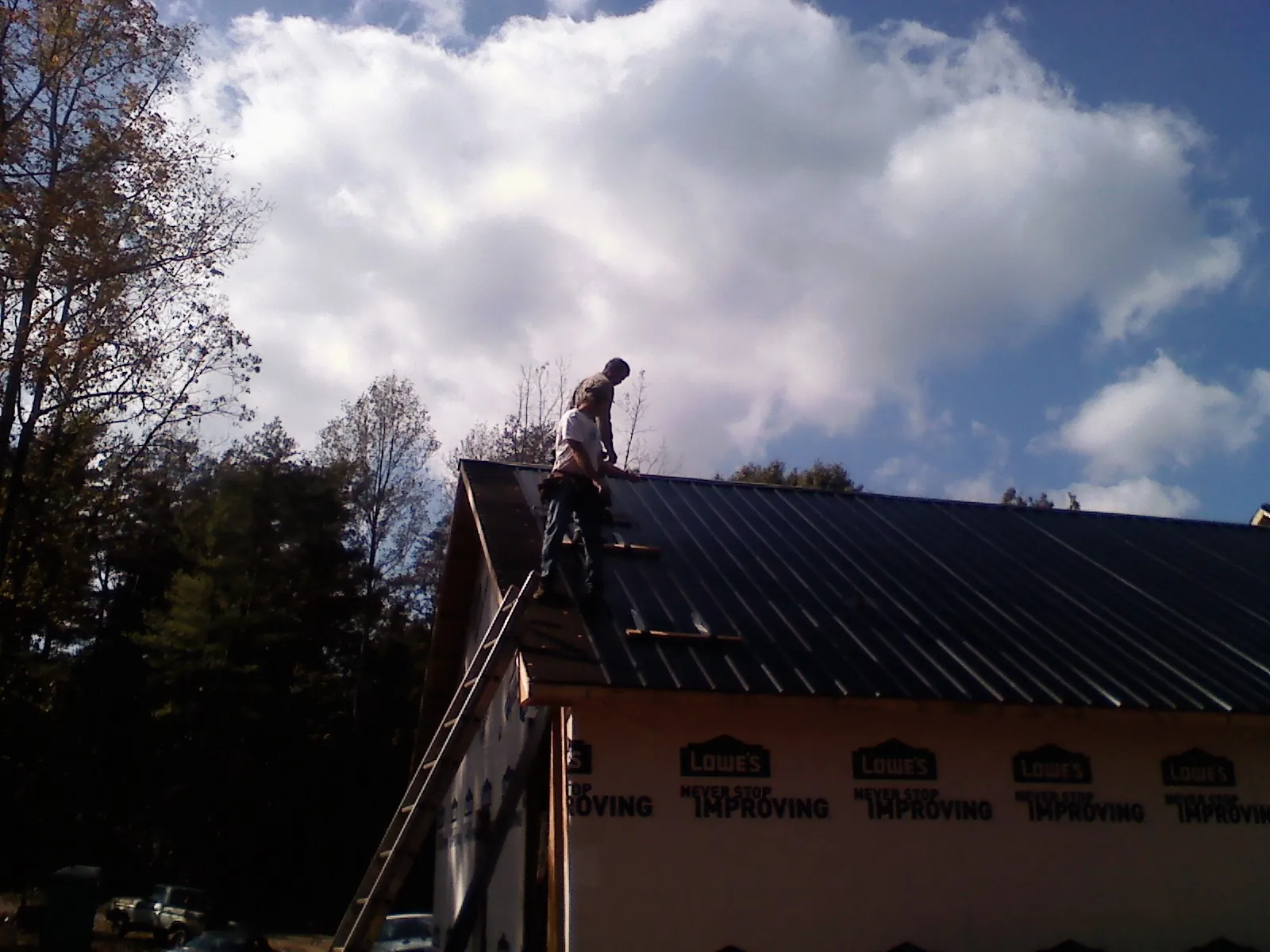 Roofer fastening dark metal panels high against a cloudy sky, from a Roof Inspection job in Urbana