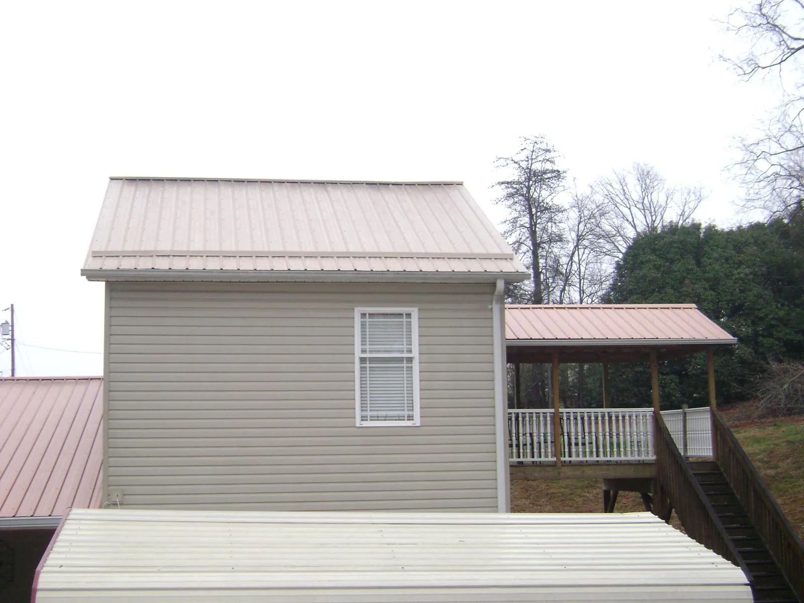 Tan metal roofs on a two story addition and attached porch, from a Roof Replacement job in Urbana